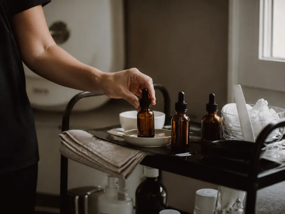 Facialist reaching for a serum bottle on a treatment trolley
